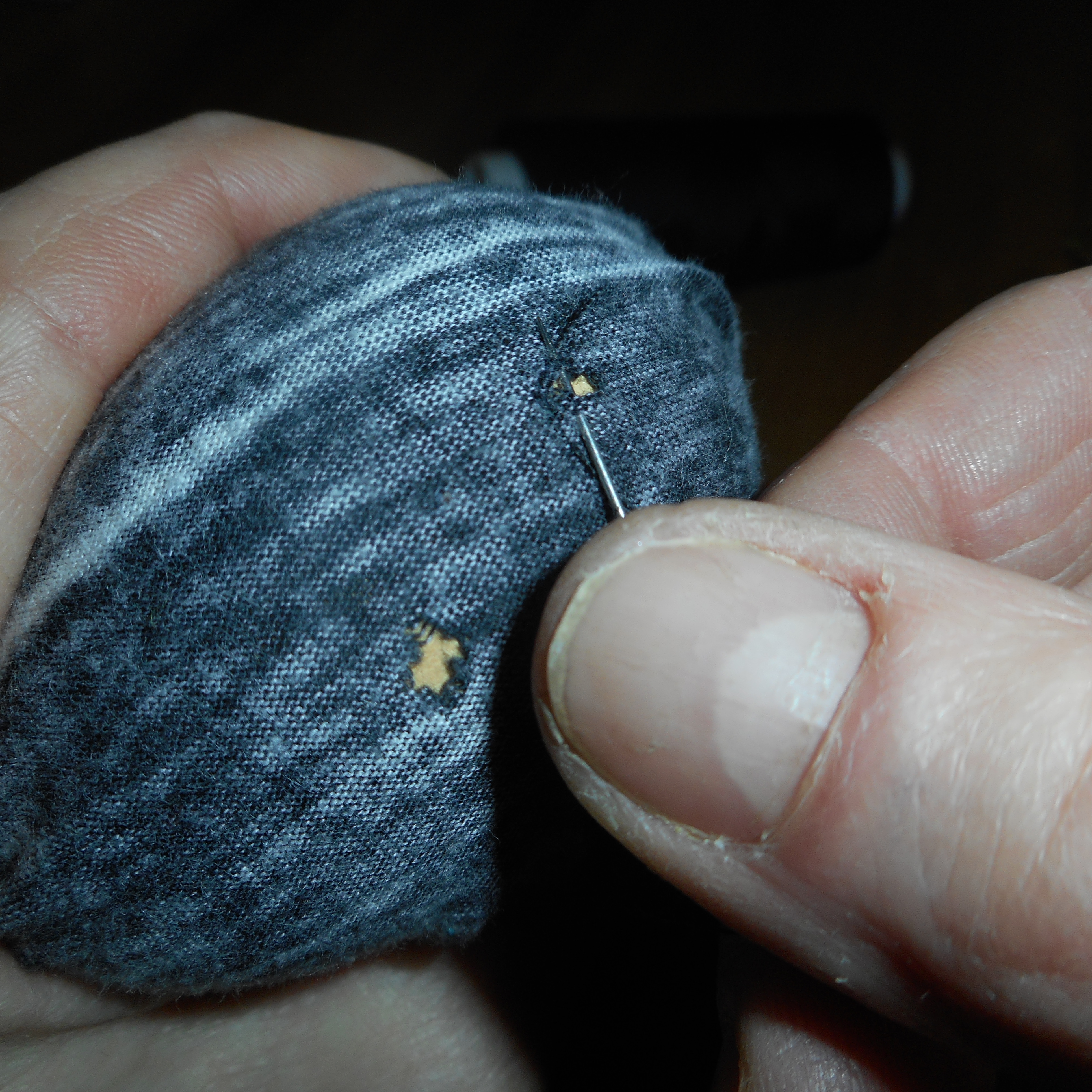 Hands hold fabric over a darning mushroom as a needle works beside a small hole.