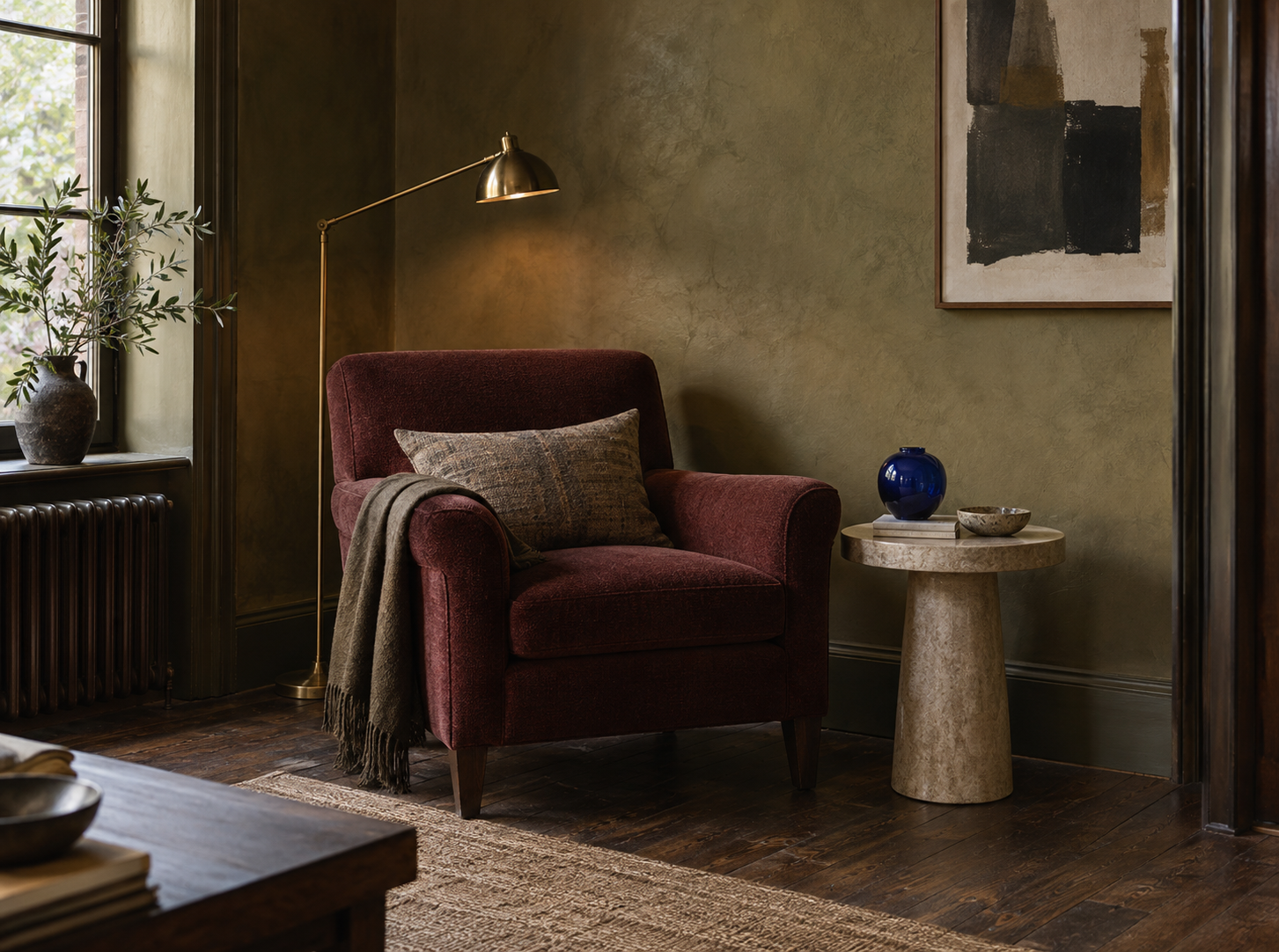 Conceptual AI reading corner with an olive wall, oxblood chair, brass lamp, stone table and cobalt vessel.