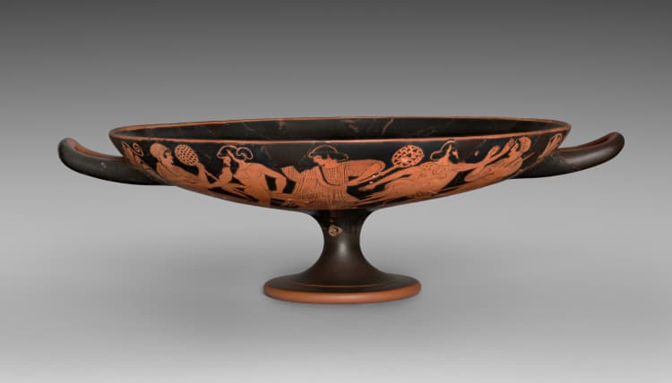 Painted figures extend around a shallow red-figure drinking cup with two handles and a raised foot.