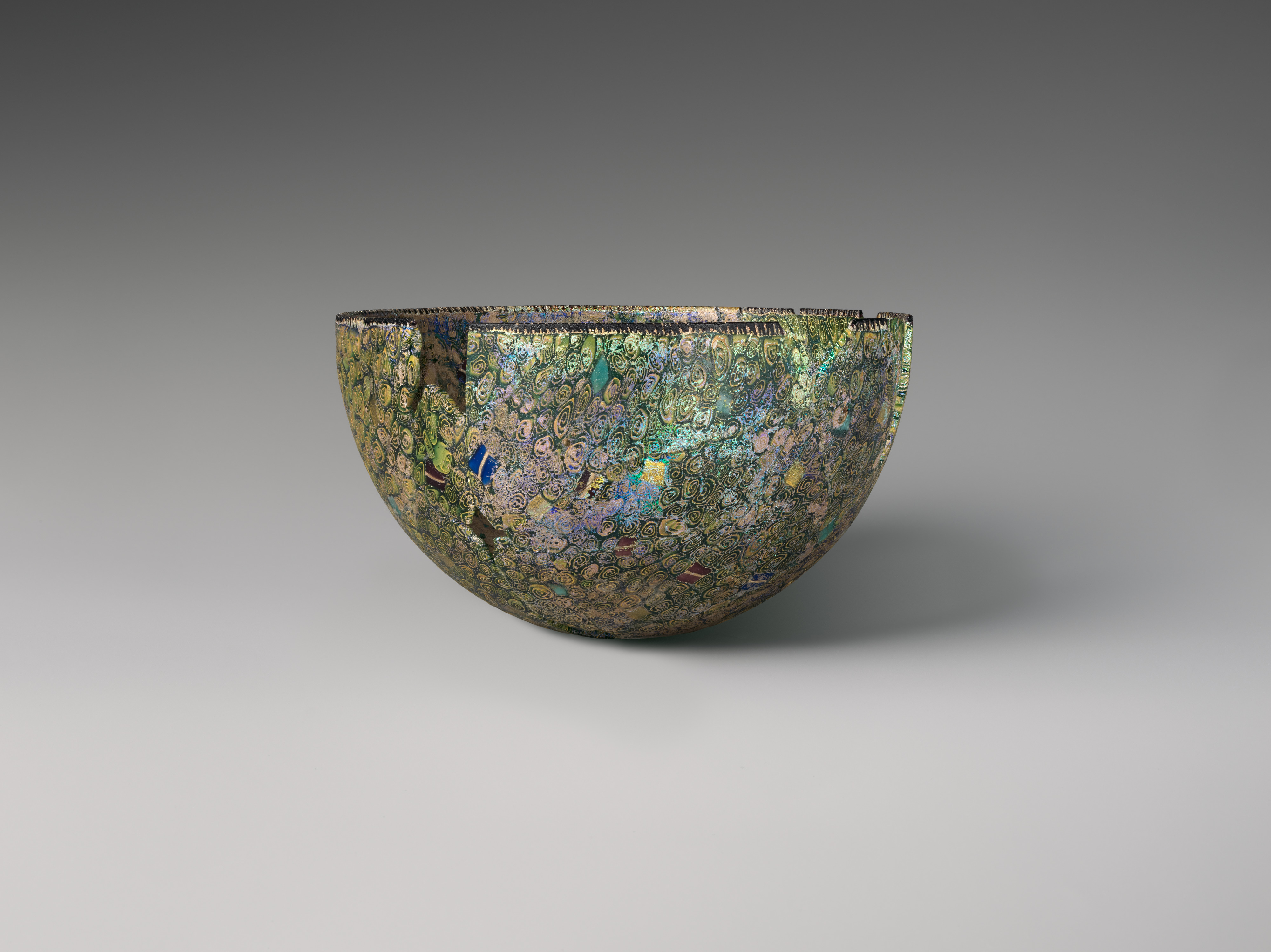 A blue, green and gold mosaic glass bowl has visible losses along its rim.